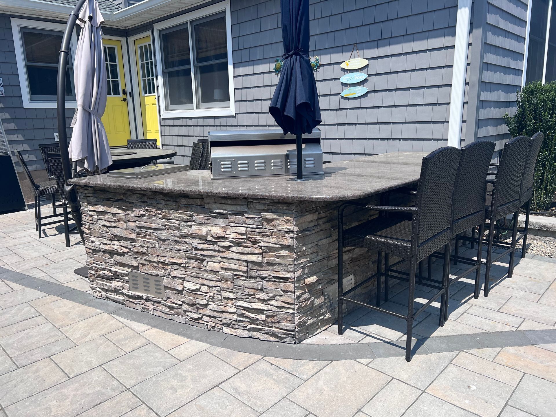 Outdoor kitchen with stone facade, granite countertop, grill, bar stools, and umbrellas.