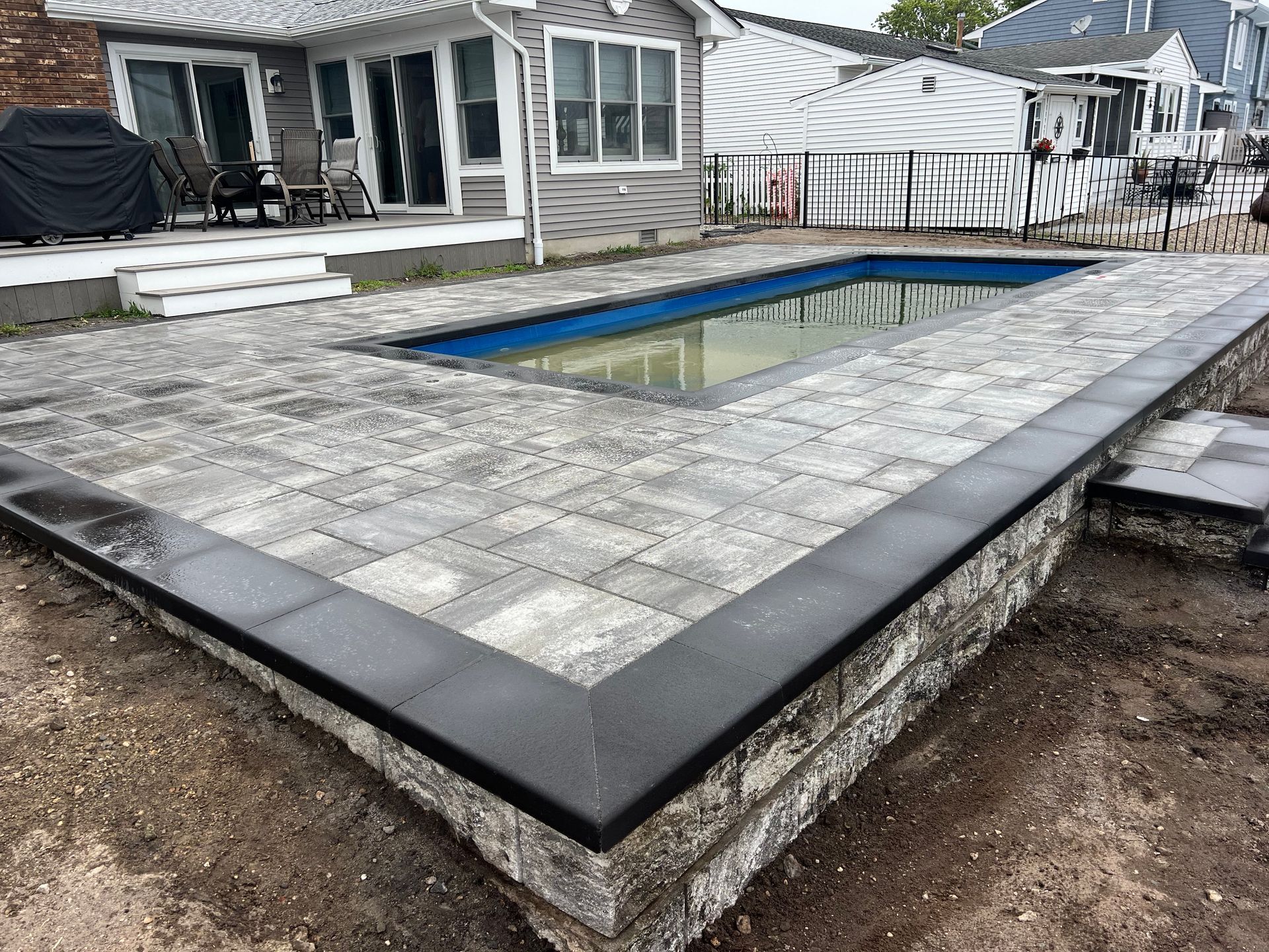 A rectangular in-ground pool surrounded by gray pavers and a low retaining wall.