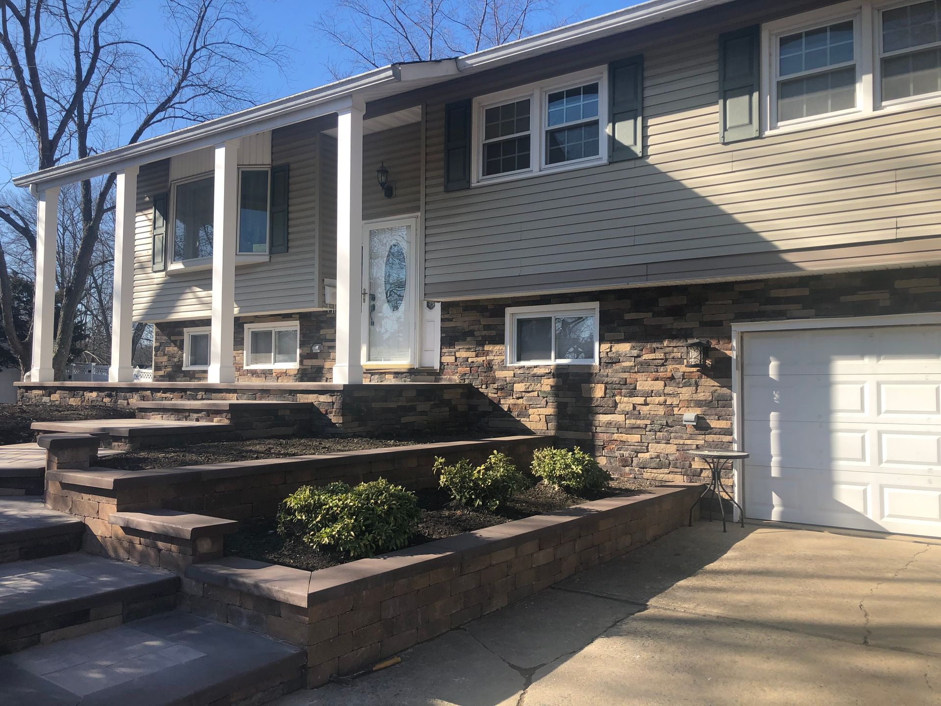 Two-story house with stone veneer and a raised porch with a white door, brown stone steps, and a driveway.