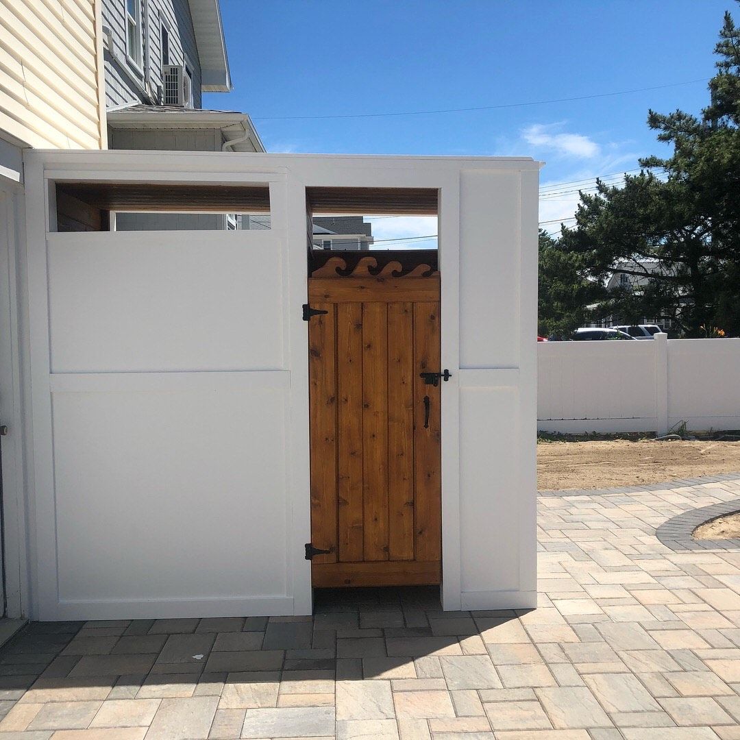 White fenced enclosure with wooden gate on a brick patio. Sunny outdoor setting.