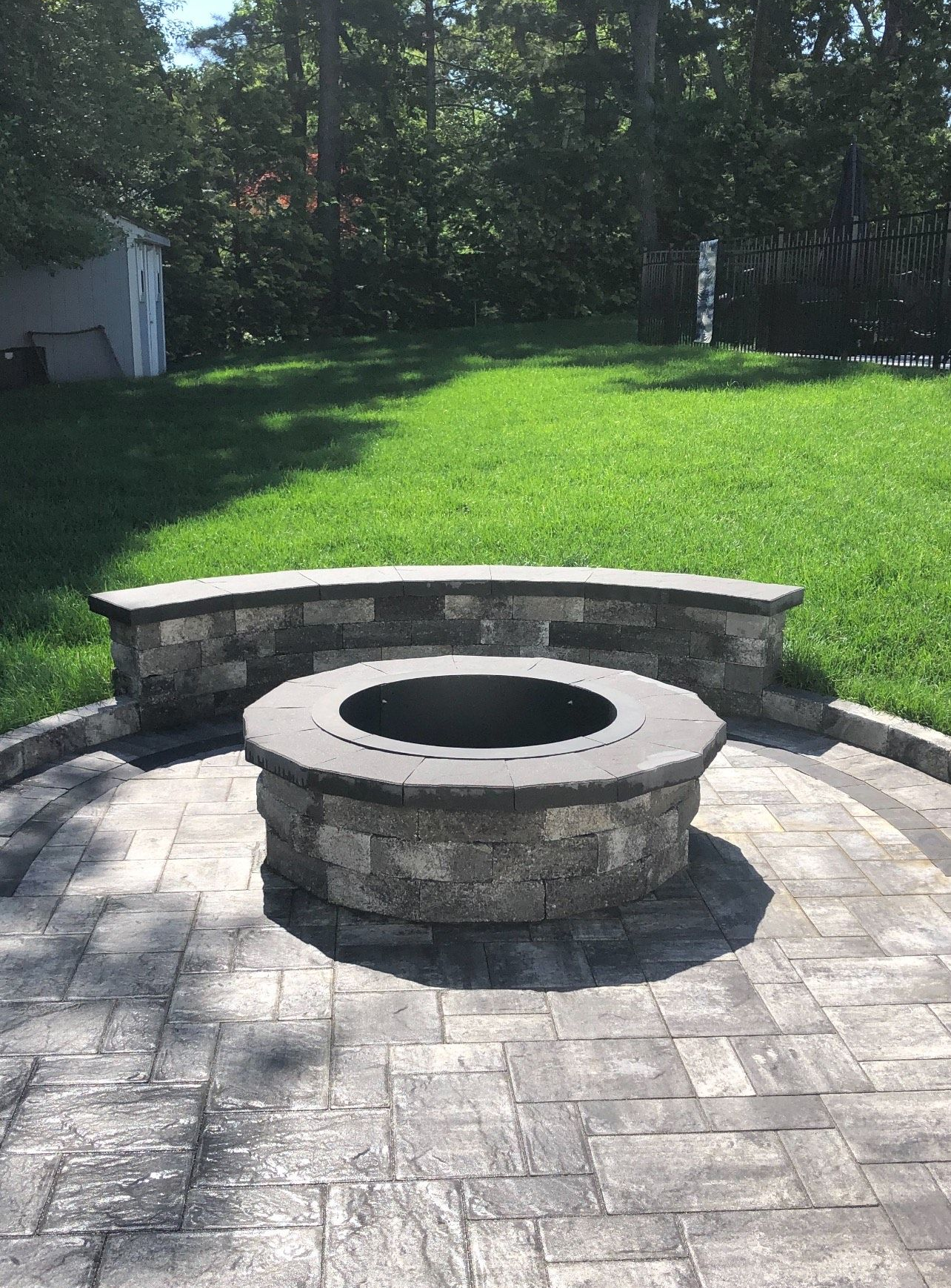 Fire pit on a stone patio with a curved stone bench in a backyard.