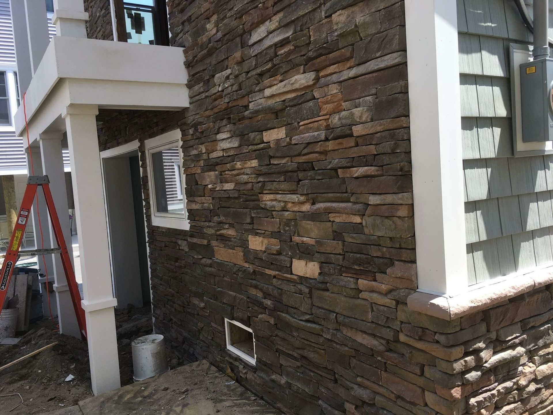 Stone veneer siding on a building exterior with white trim, a small window, and a gray electrical box.