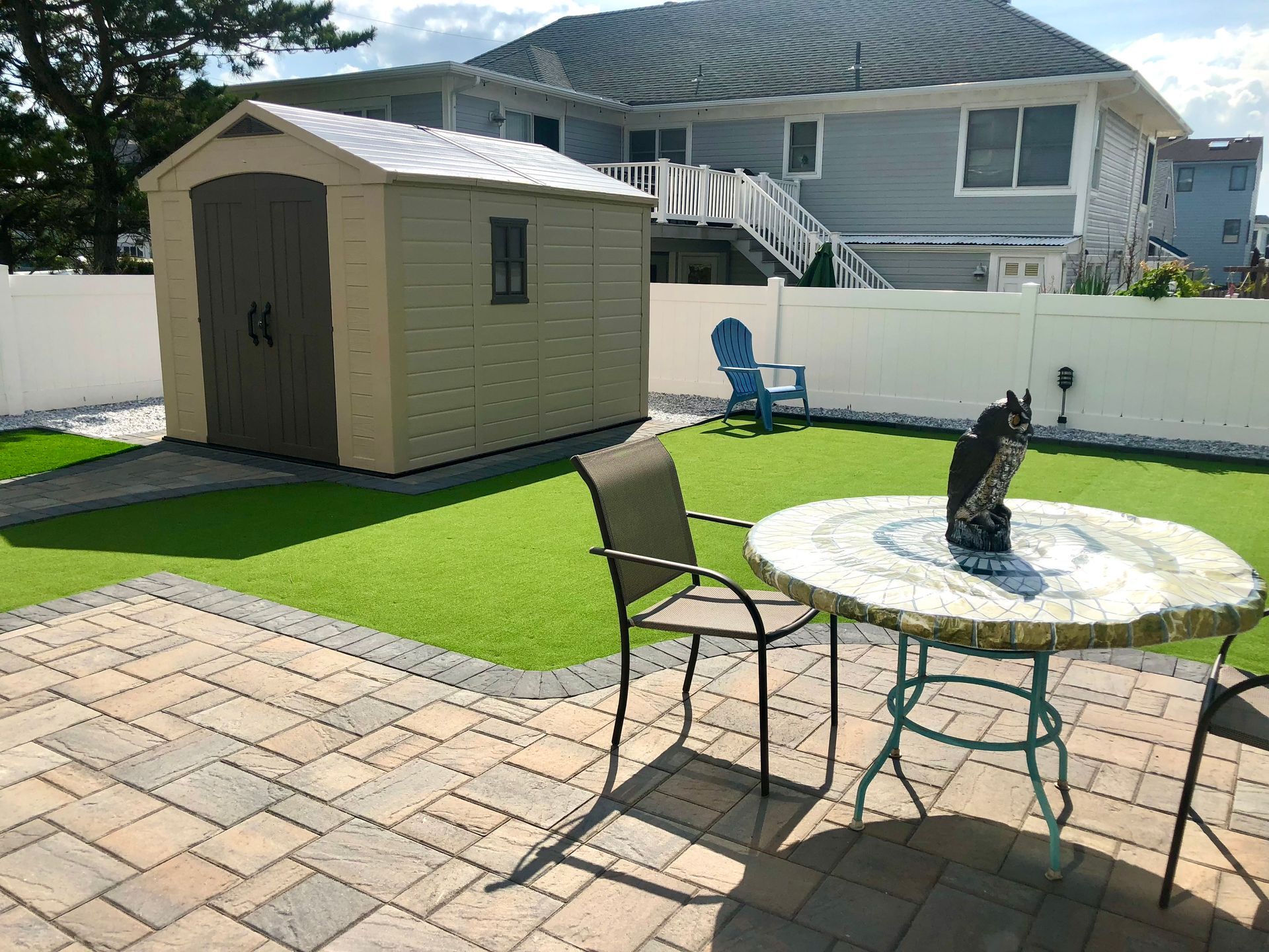 A backyard with a shed, patio table, and artificial turf, surrounded by a white fence.