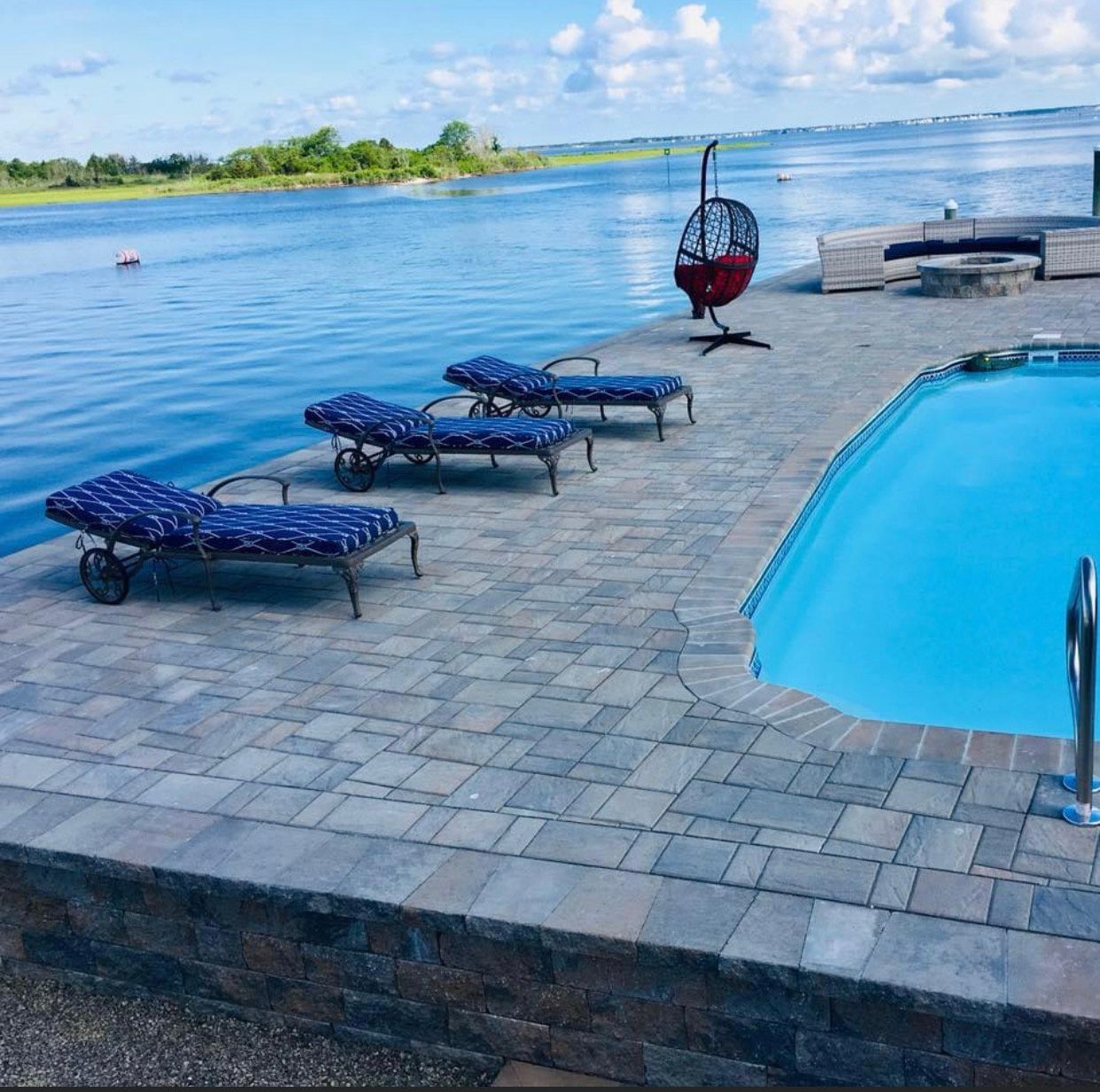Poolside with lounge chairs overlooking a body of water on a sunny day.