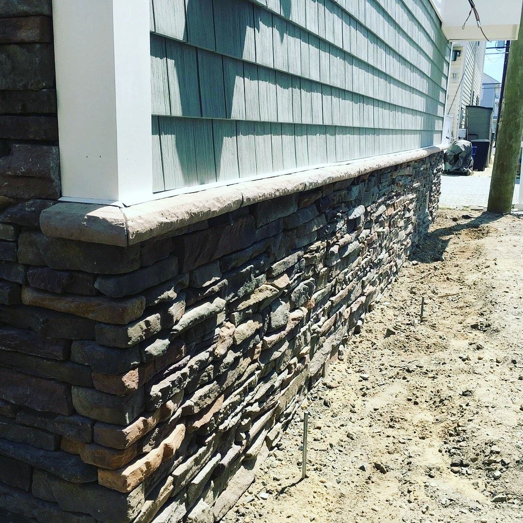 Stone veneer foundation with green shingle siding and white trim.