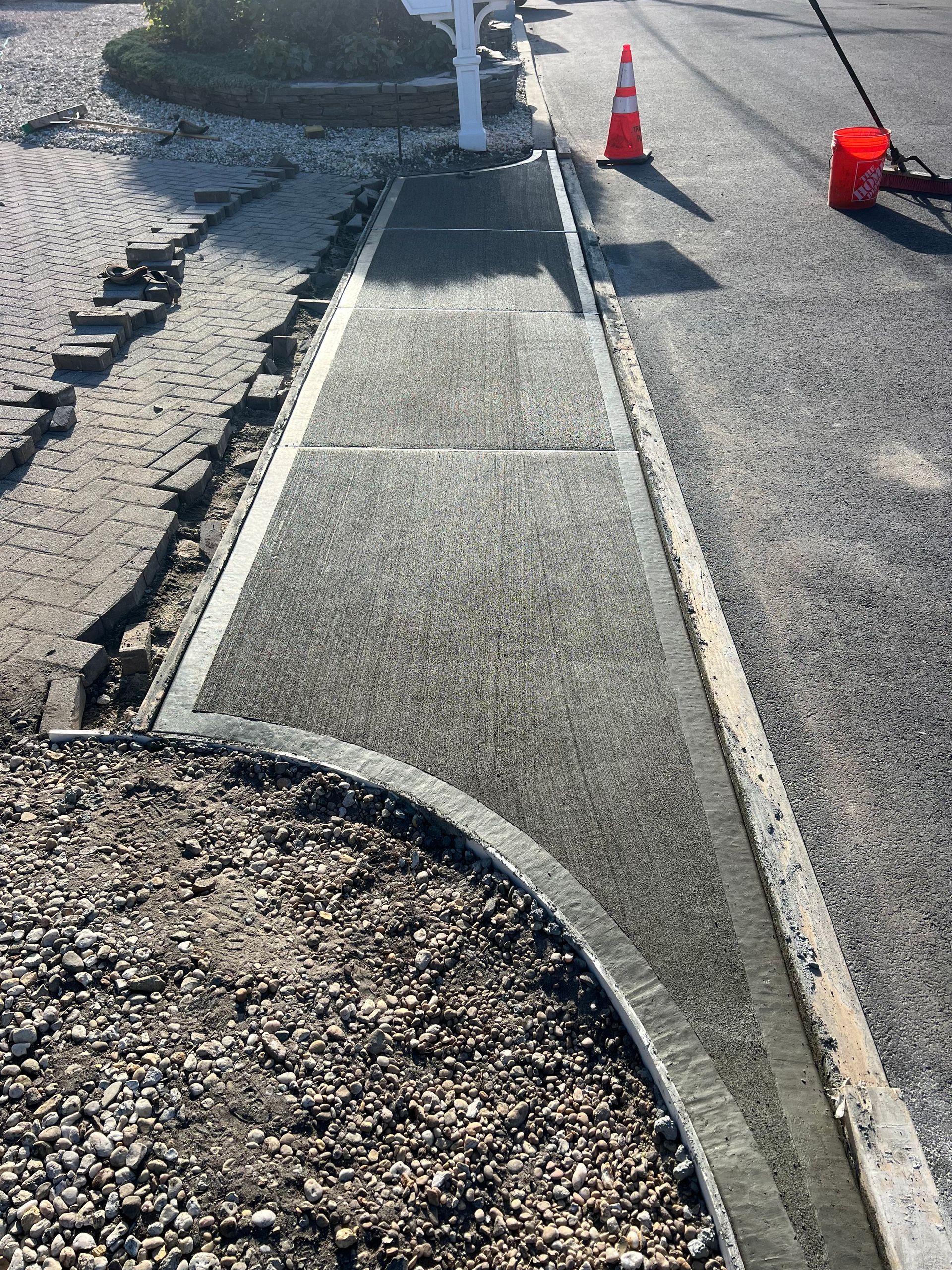 New concrete sidewalk being installed next to a driveway and landscaping.