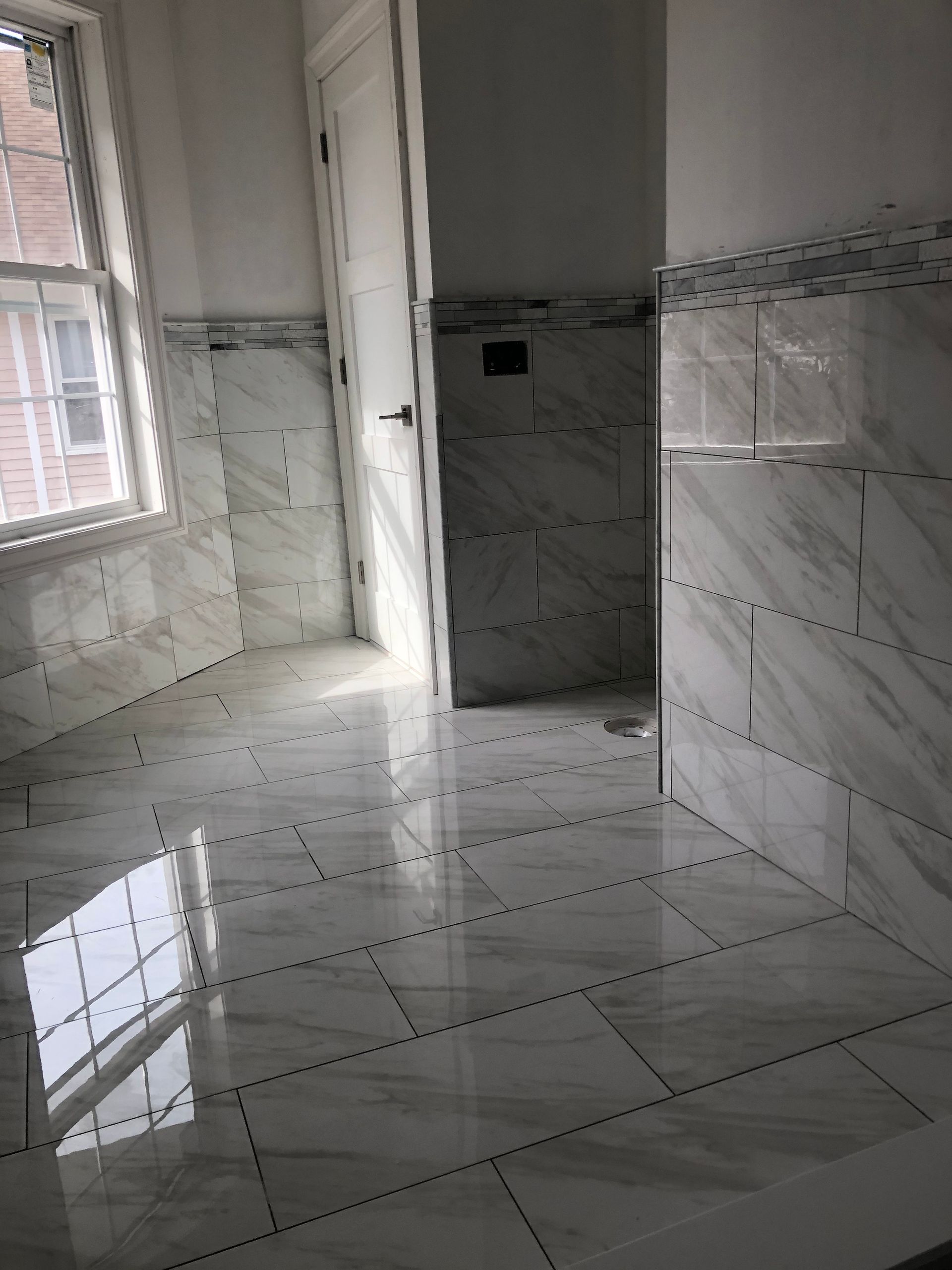 Newly tiled bathroom with large white tiles, window, door, and shower.