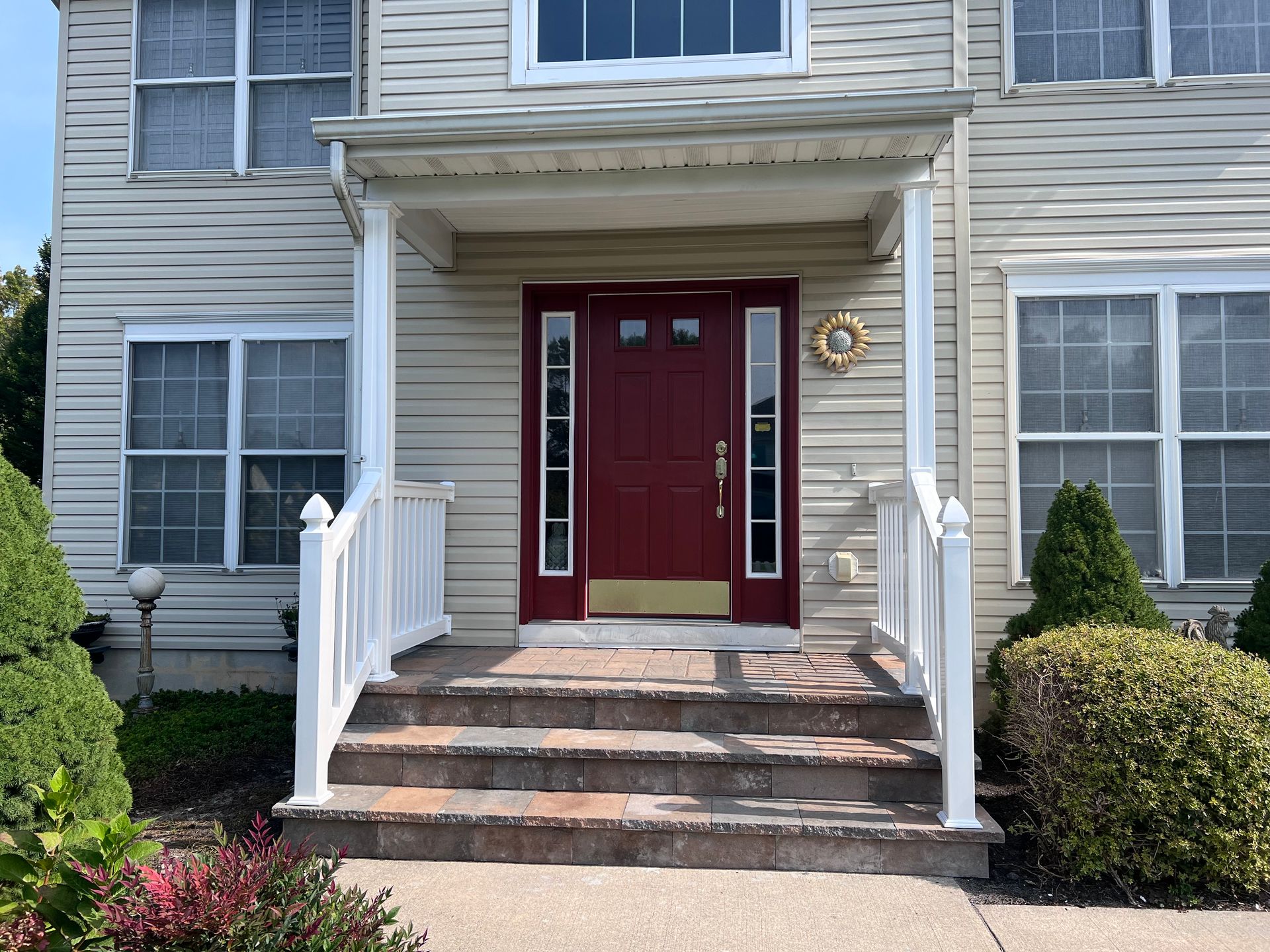 Beige house with a burgundy front door, white porch, and steps.