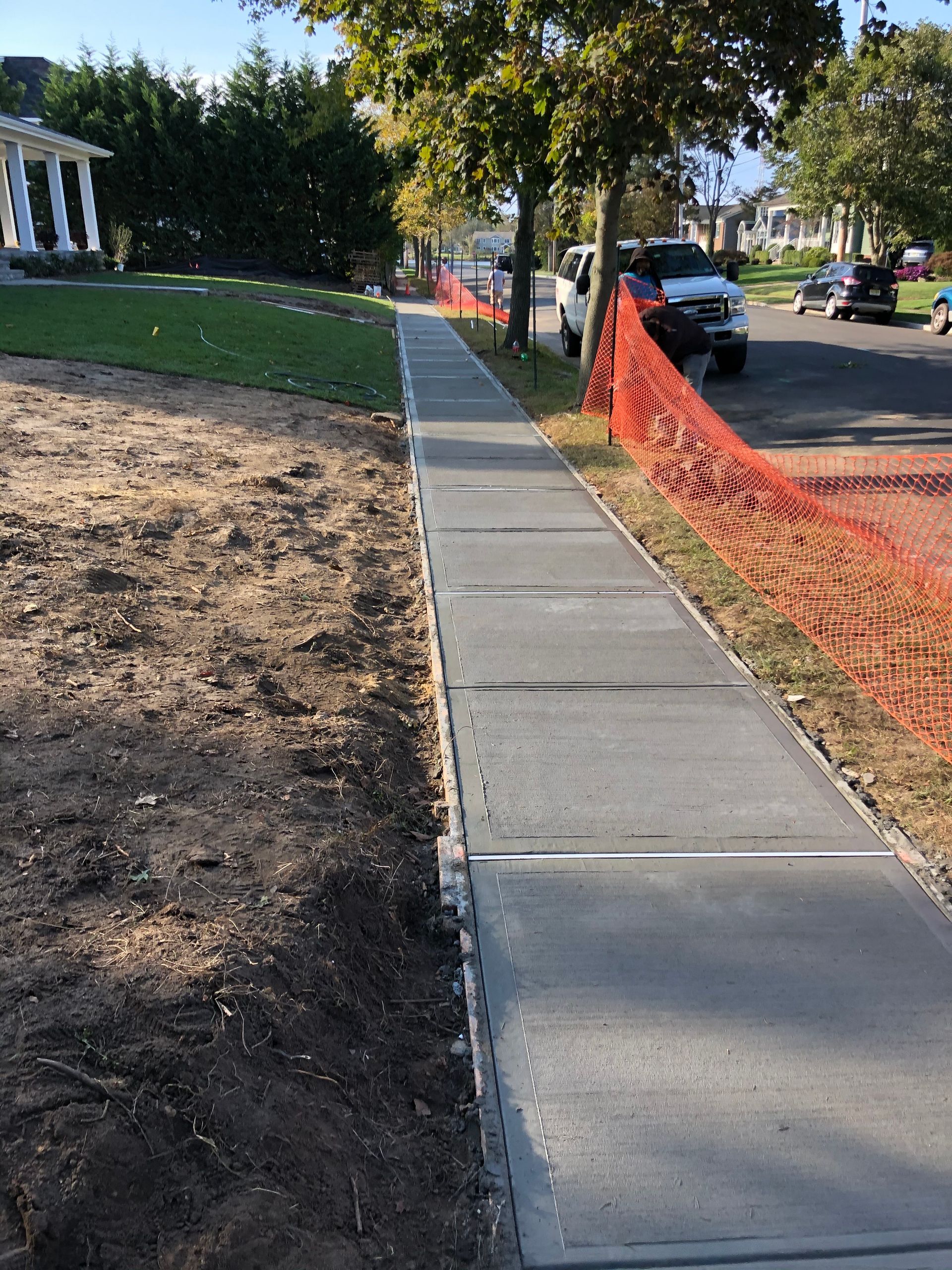 Newly poured concrete sidewalk with orange safety fencing alongside.