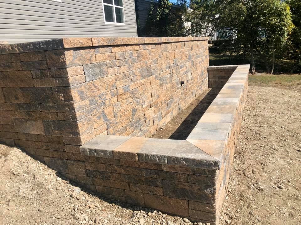 Stone retaining wall, likely new construction, with built-in planter; tan and gray blocks, outdoors.
