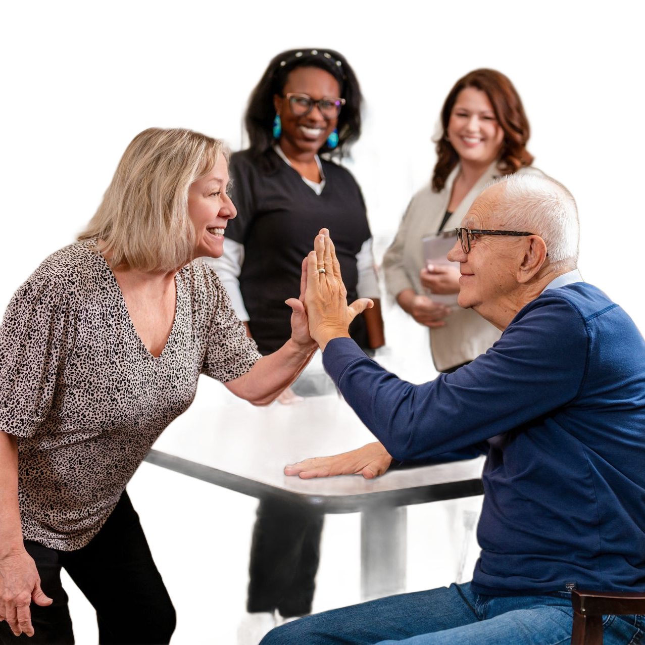 Two people high-fiving over a table; two other people watch and smile. Indoor setting.