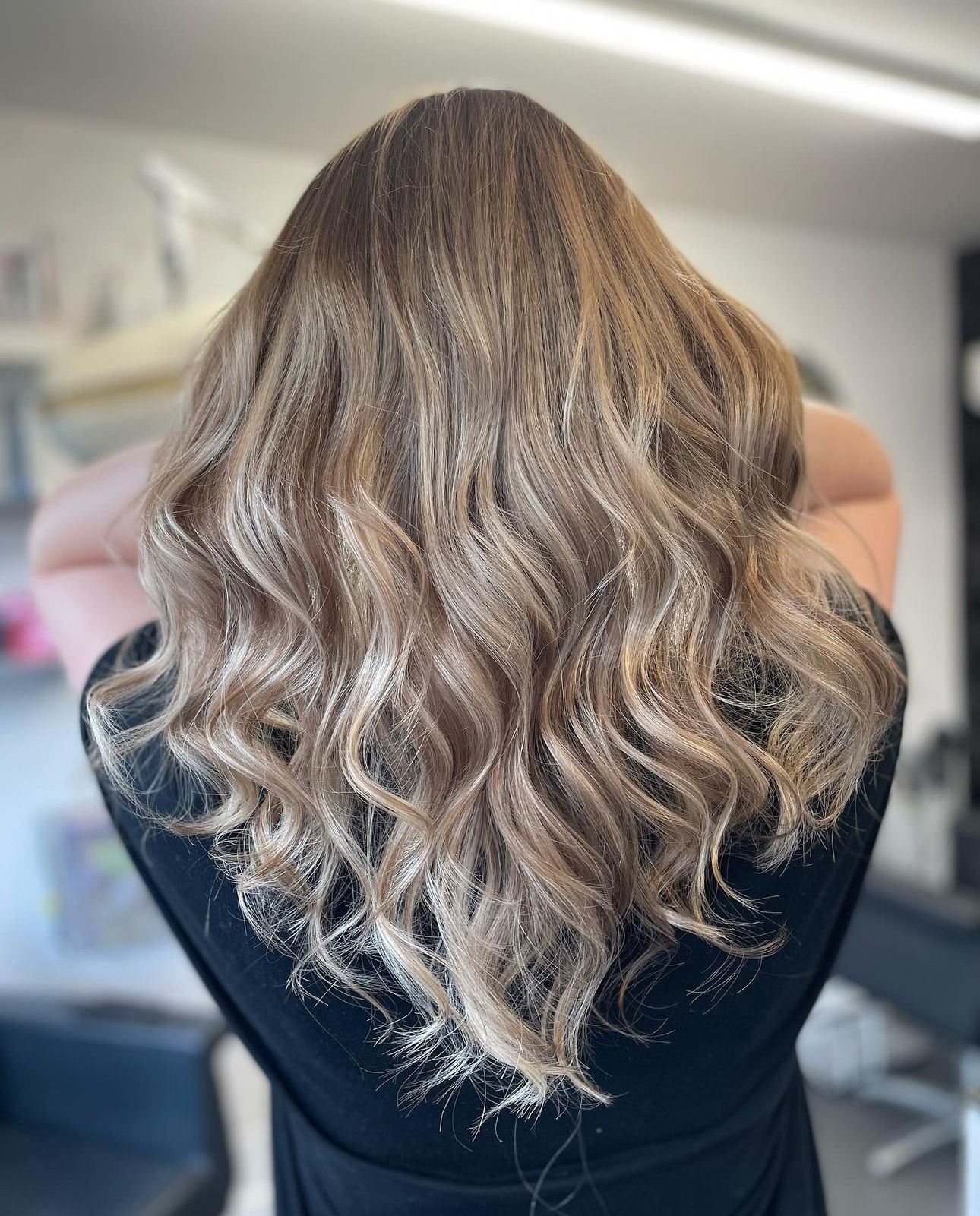 A woman with long wavy blonde hair is standing in a salon.