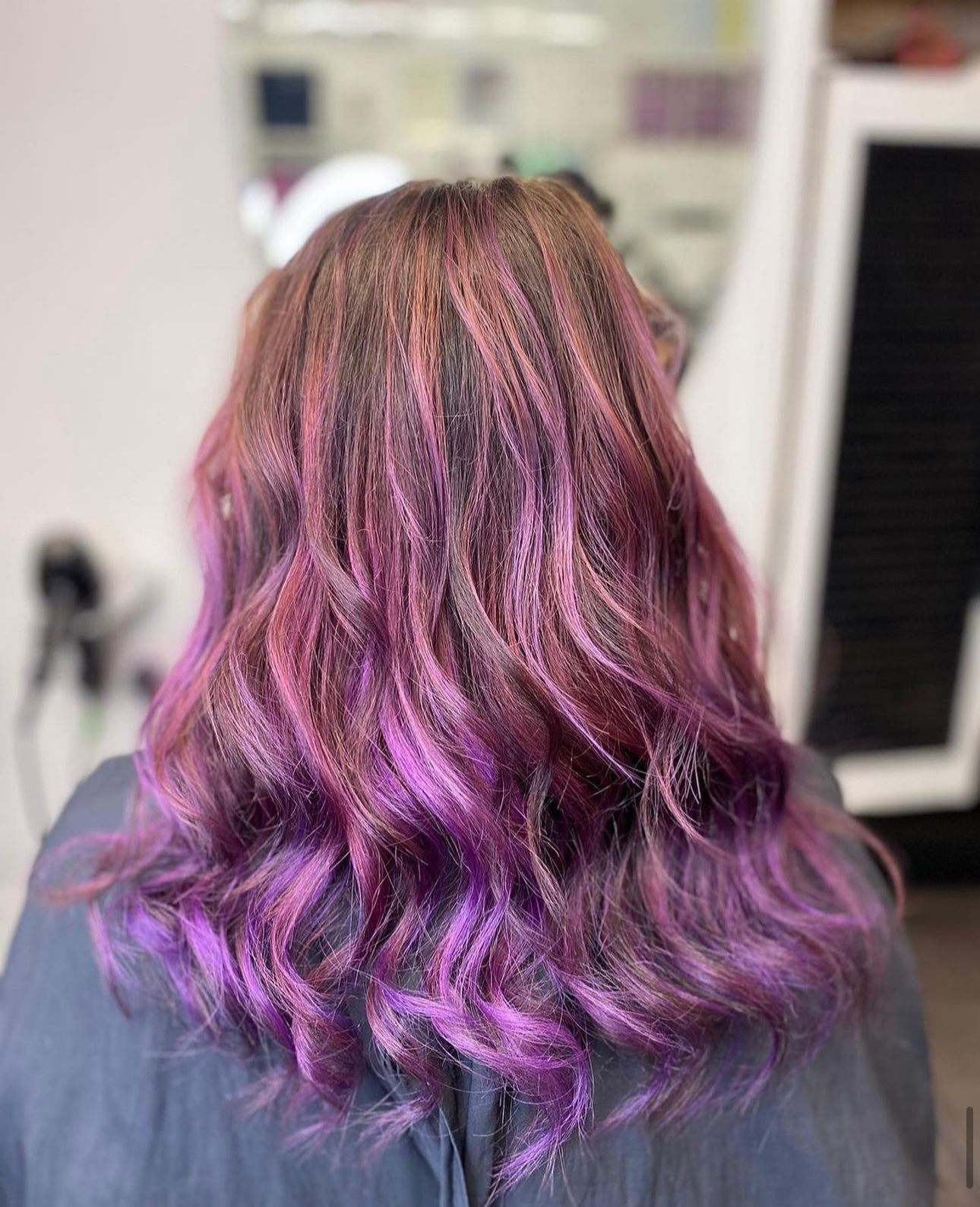 A woman with purple hair is getting her hair dyed in a salon.