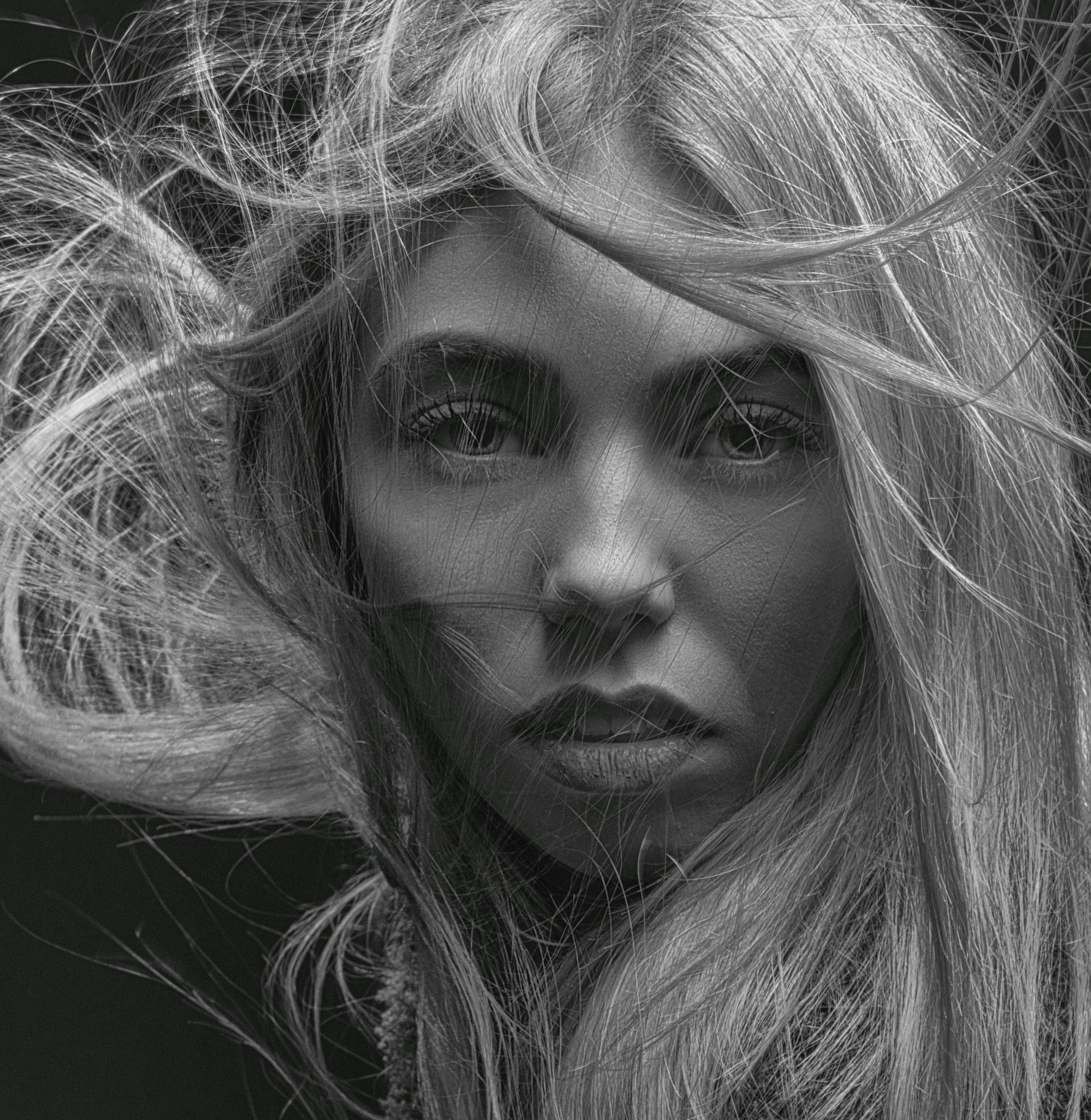 A black and white photo of a woman with long hair blowing in the wind.