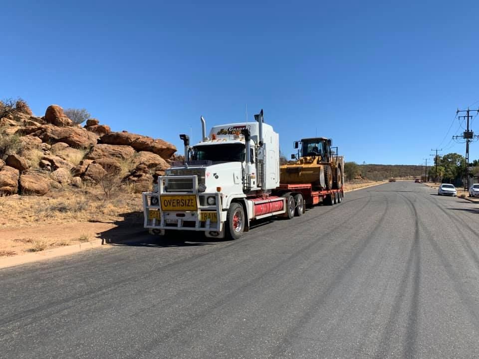 A semi truck is driving down a road with a bulldozer on the back. — Territory Towing & Transport In Alice Springs, NT