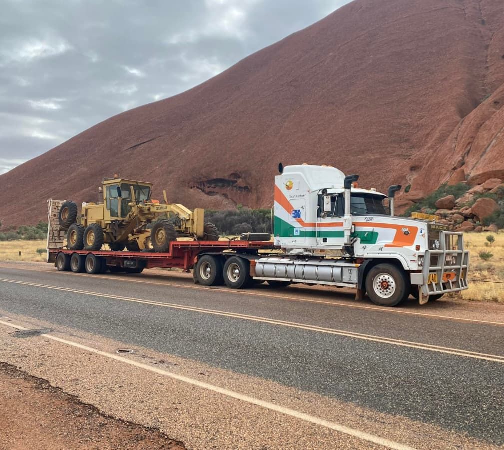 A Semi Truck Is Carrying A Bulldozer Down A Road — Territory Towing & Transport In Alice Springs, NT