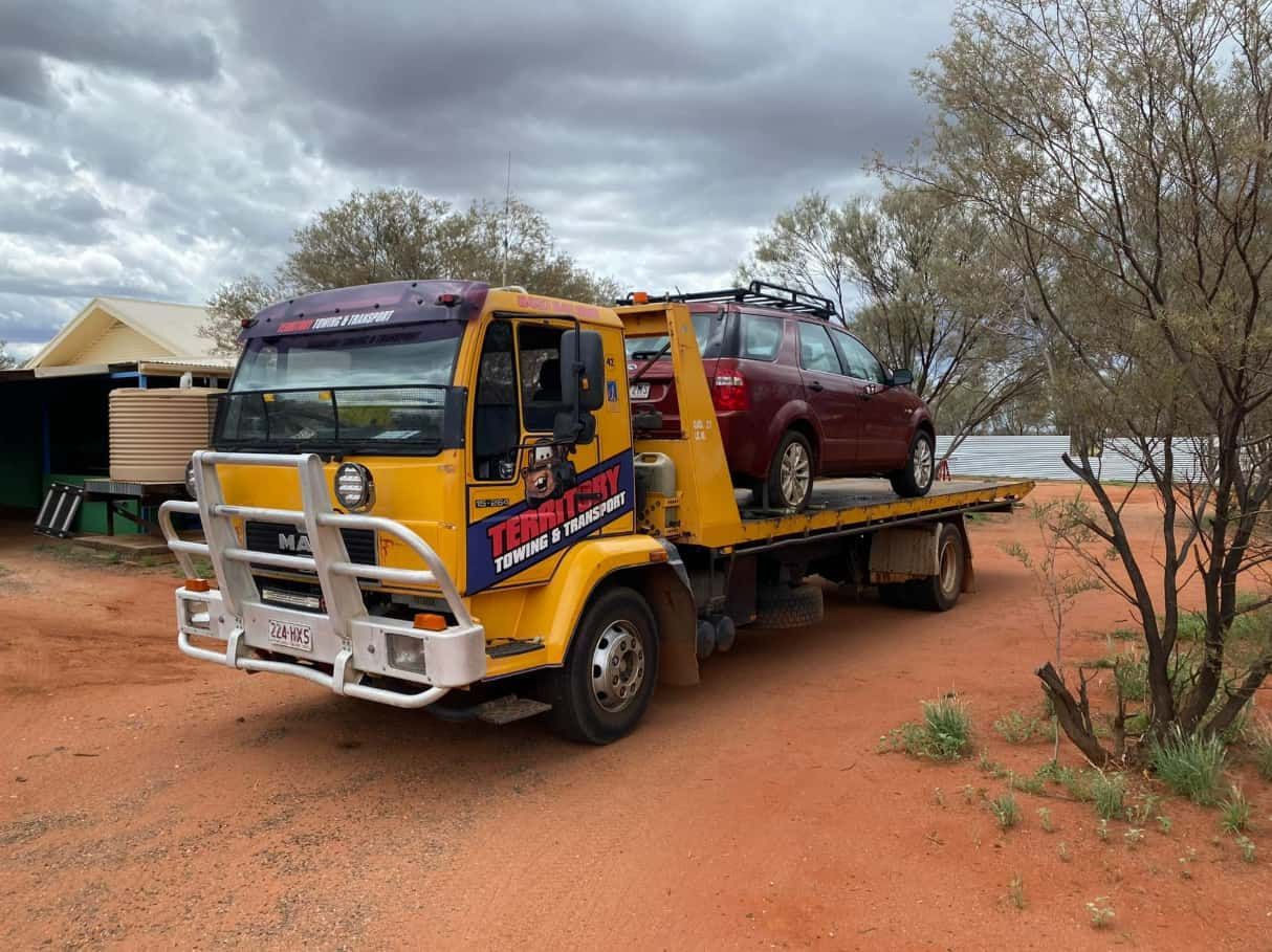A Yellow Tow Truck Is Carrying A Red Car On Its Flatbed — Territory Towing & Transport In Alice Springs, NT