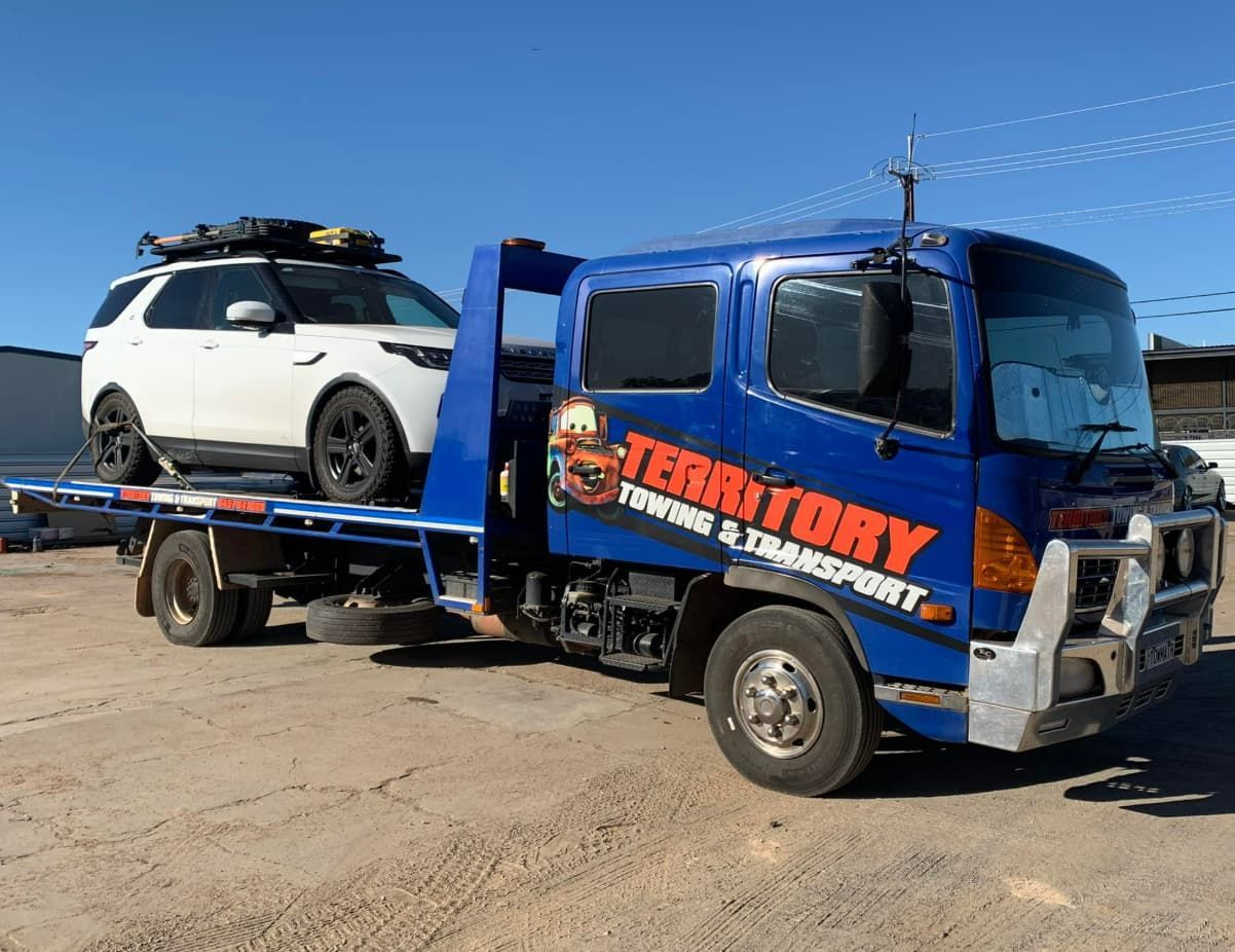 A Blue Tow Truck With A White Suv On The Back Is Parked In A Dirt Lot — Territory Towing & Transport In Alice Springs, NT