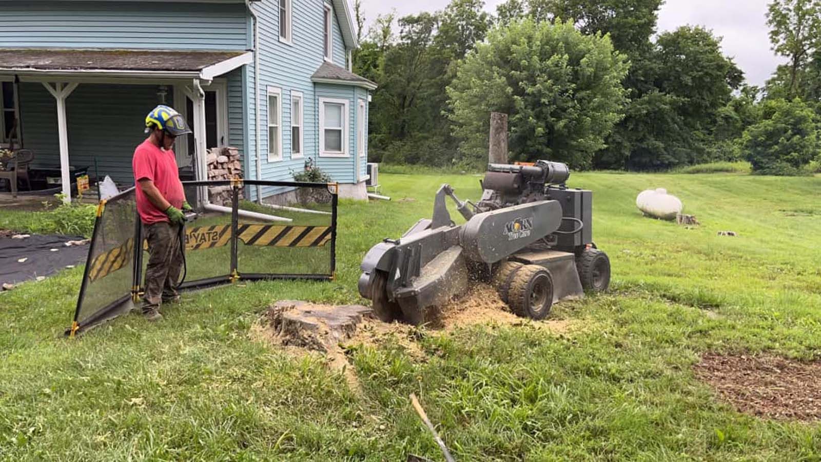 A man is using a stump grinder to remove a tree stump in front of a house.