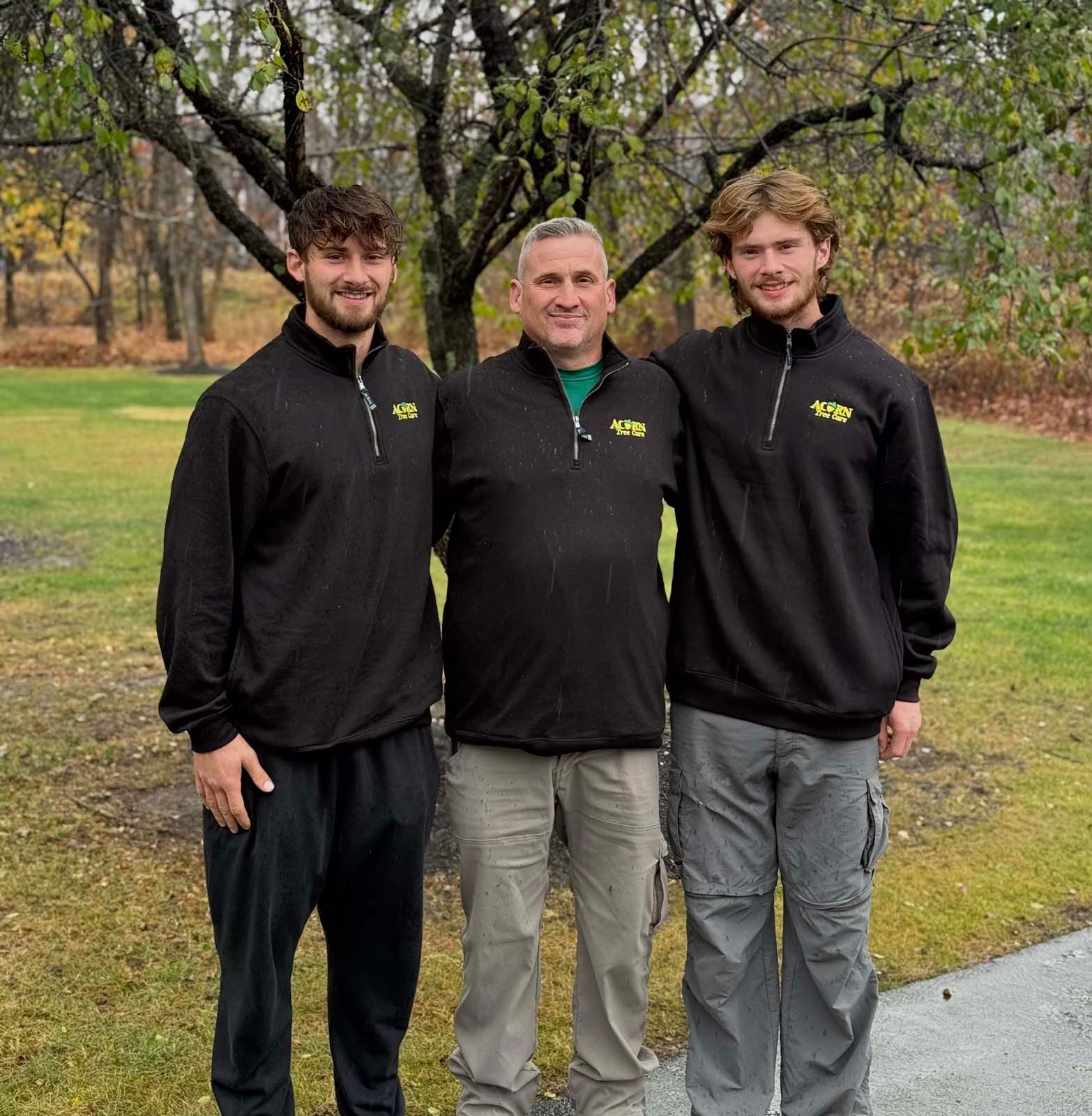 Three men are posing for a picture in front of a tree