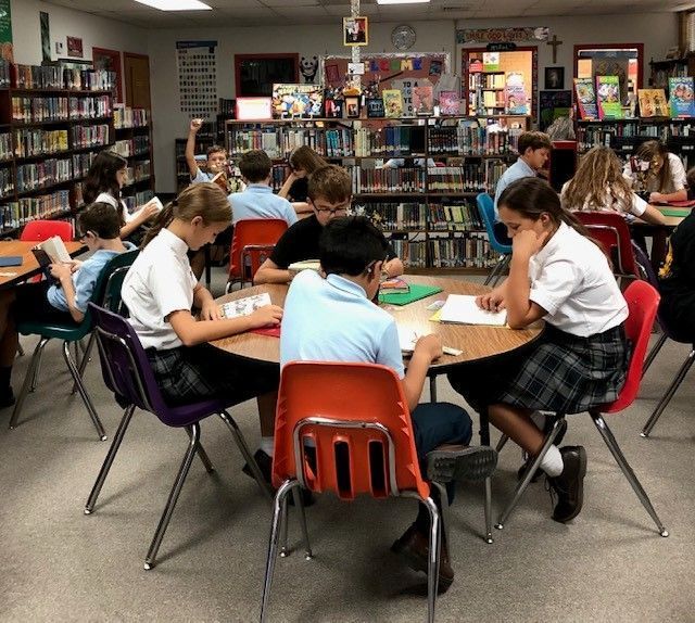 a group of children sit around a table in a library