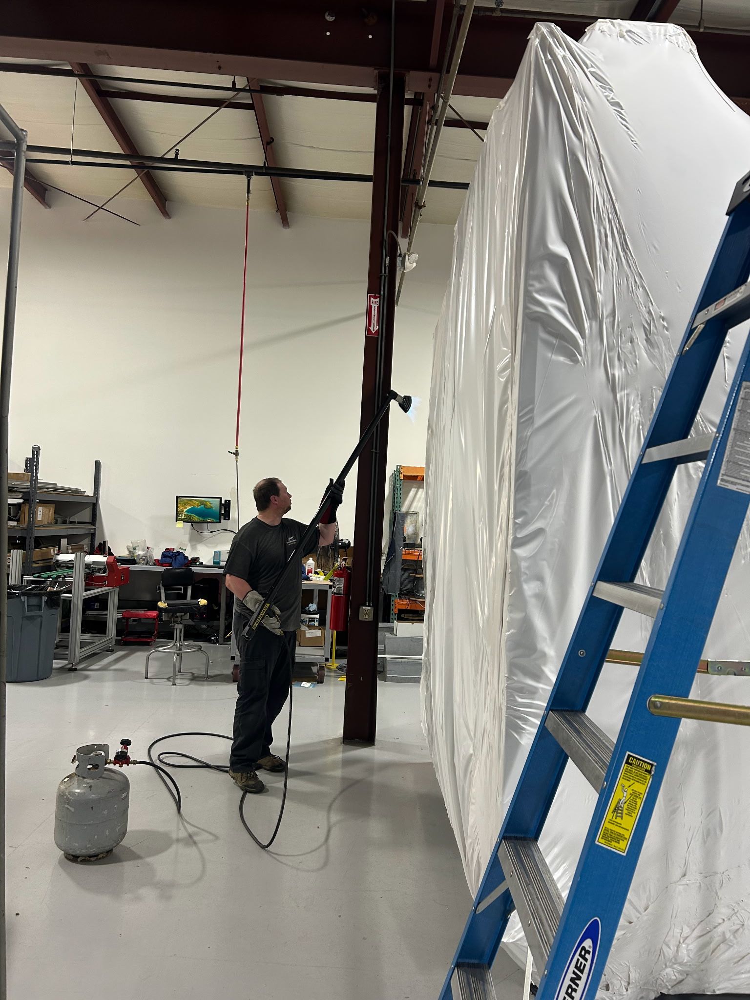 A man is standing next to a blue ladder in a factory.