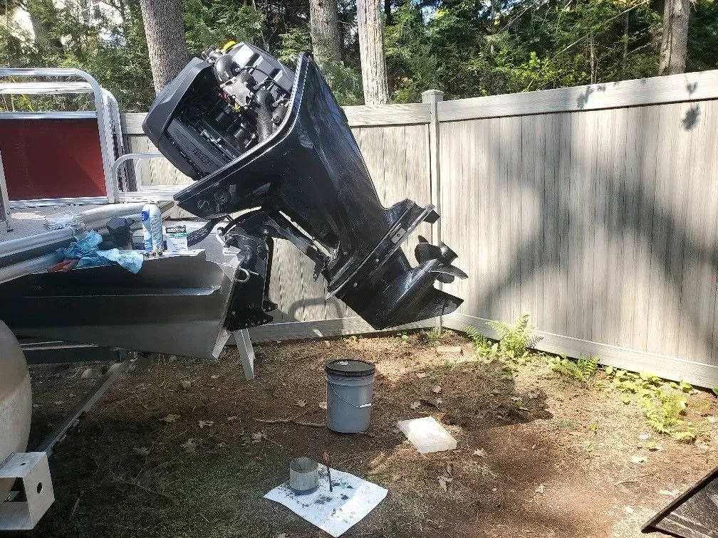 A boat engine is sitting on the ground next to a fence.