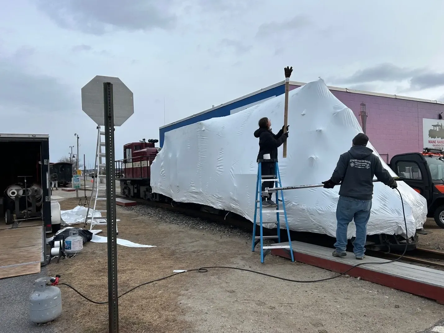 Two men are wrapping a train car in plastic wrap.