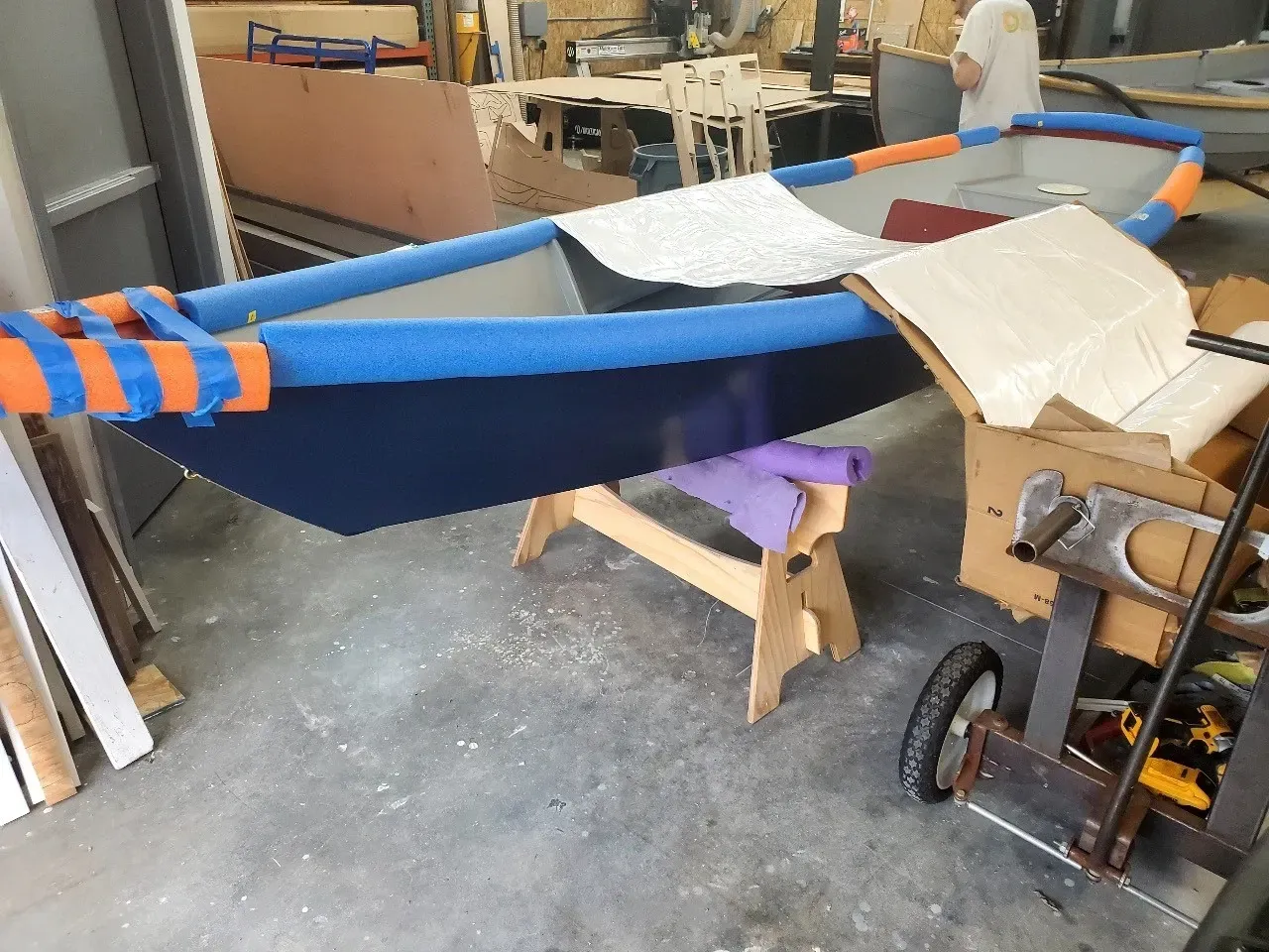 A blue and orange boat is being built in a garage