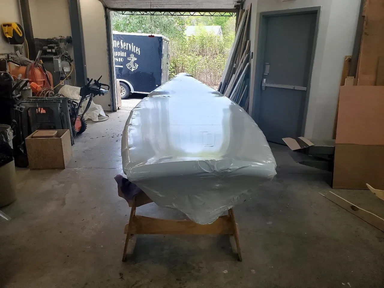 A surfboard is wrapped in plastic and sitting on a wooden stand in a garage.