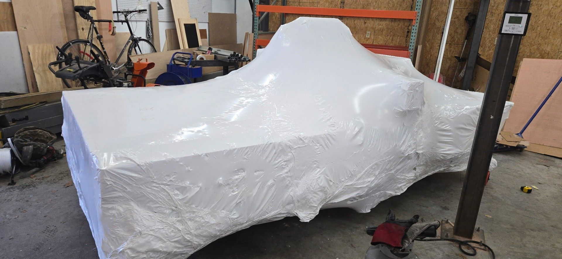 A white car, wrapped in plastic, inside a workshop.