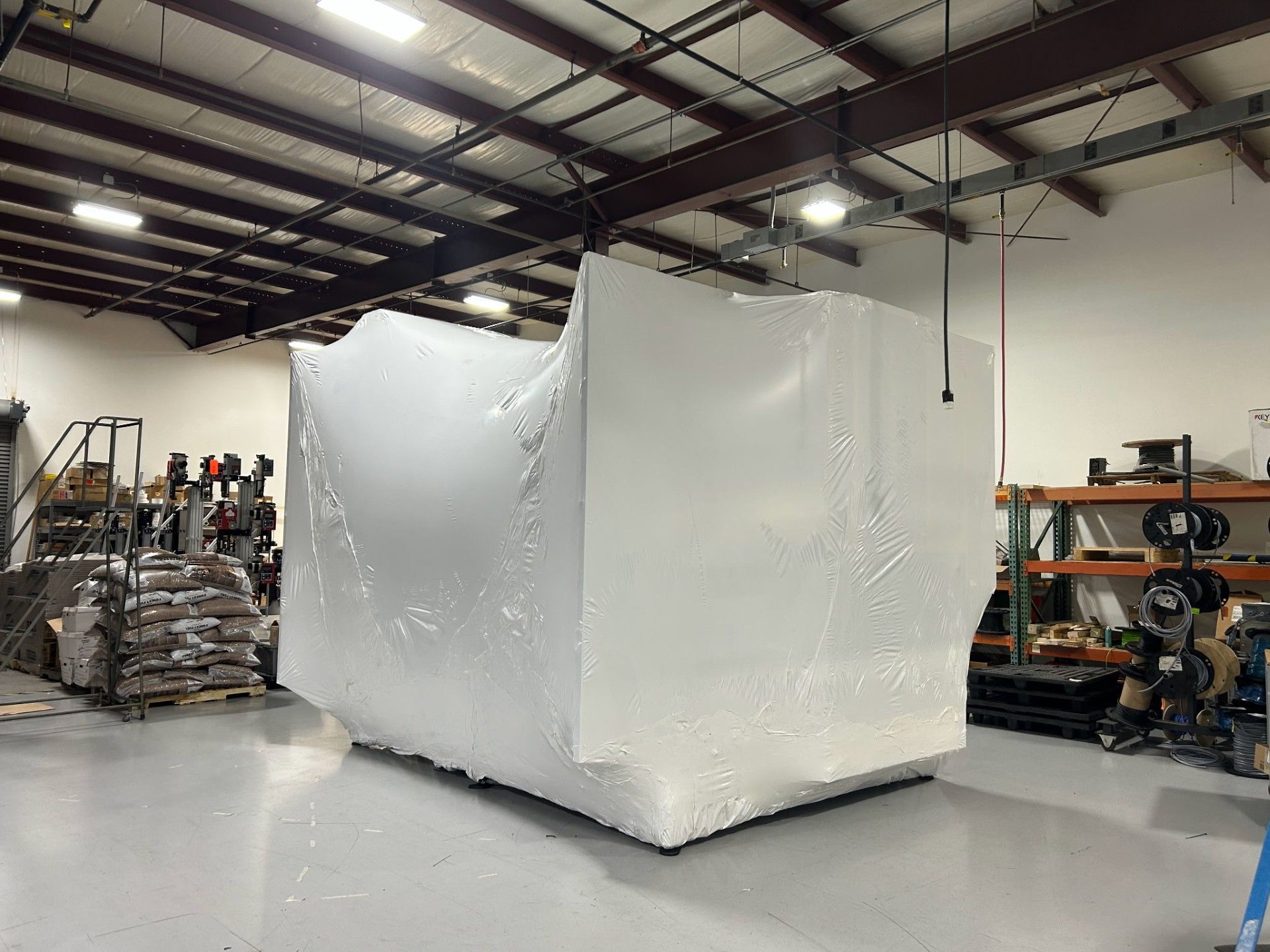 A large piece of equipment is wrapped in plastic in a warehouse.