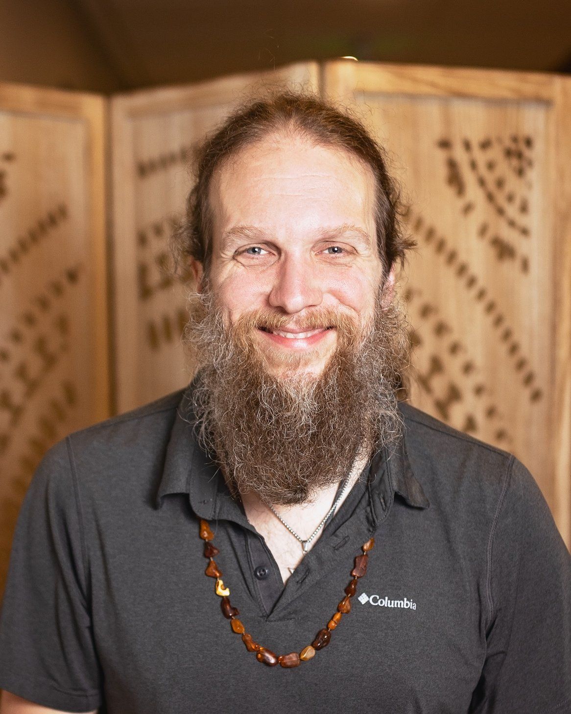 A man with a beard and a necklace is smiling for the camera.