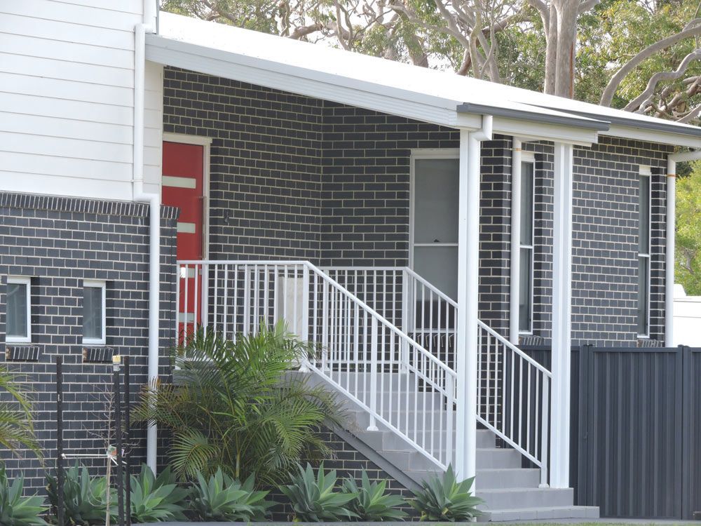 A house exterior with brick walls, a red front door, and a white-railed porch with steps.