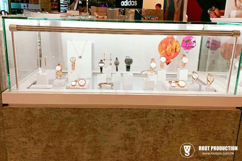 Jewelry display case with watches and necklaces on white stands. Neutral background, indoors.