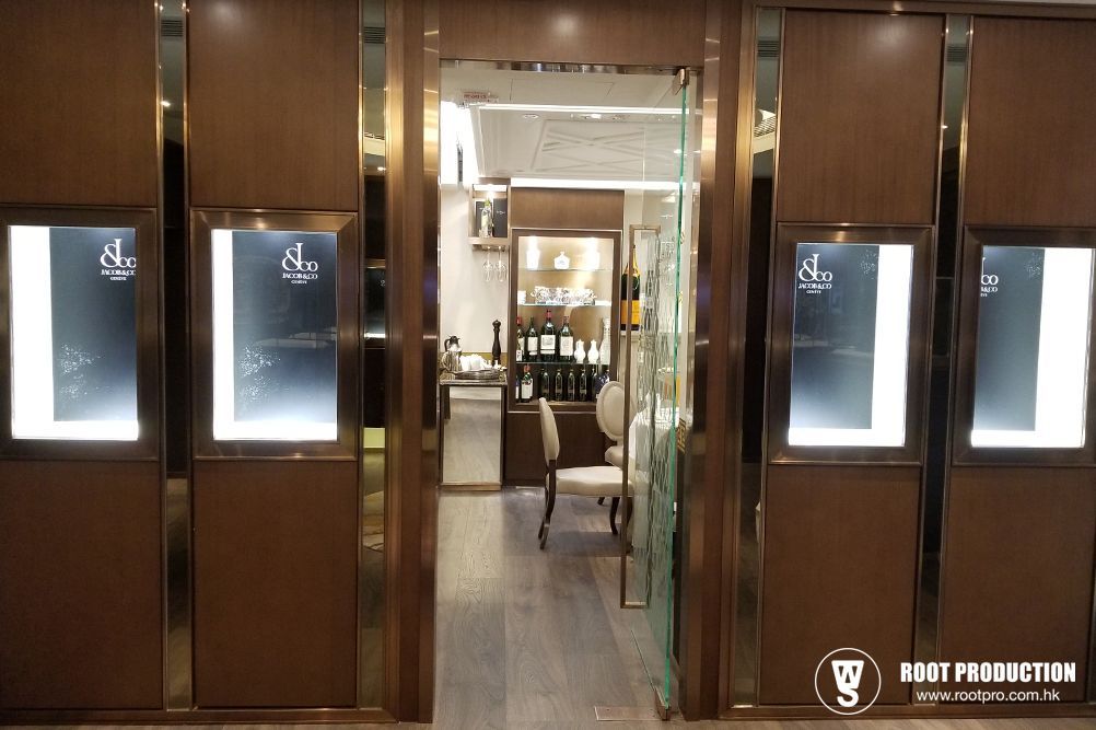 Entrance to a luxury shop with illuminated displays and a glass door leading inside. Wooden walls with gold trim.