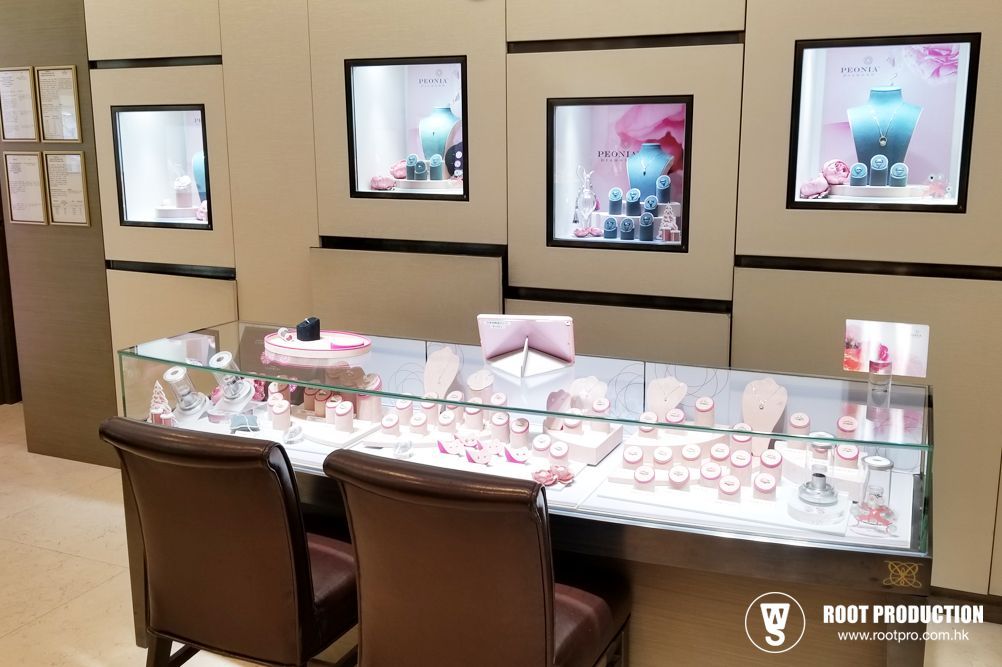 Jewelry store display with glass cases, showcases necklaces and rings. Pink accents, two brown chairs.