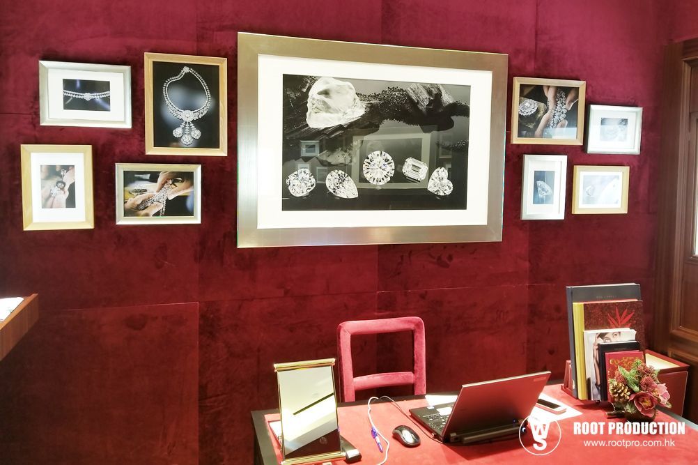Red-walled office with framed jewelry photos, desk, laptop, and pink chair.