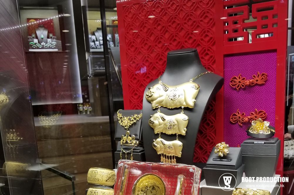 Gold jewelry display in a store window, featuring necklaces, rings, and red and pink decorative elements.