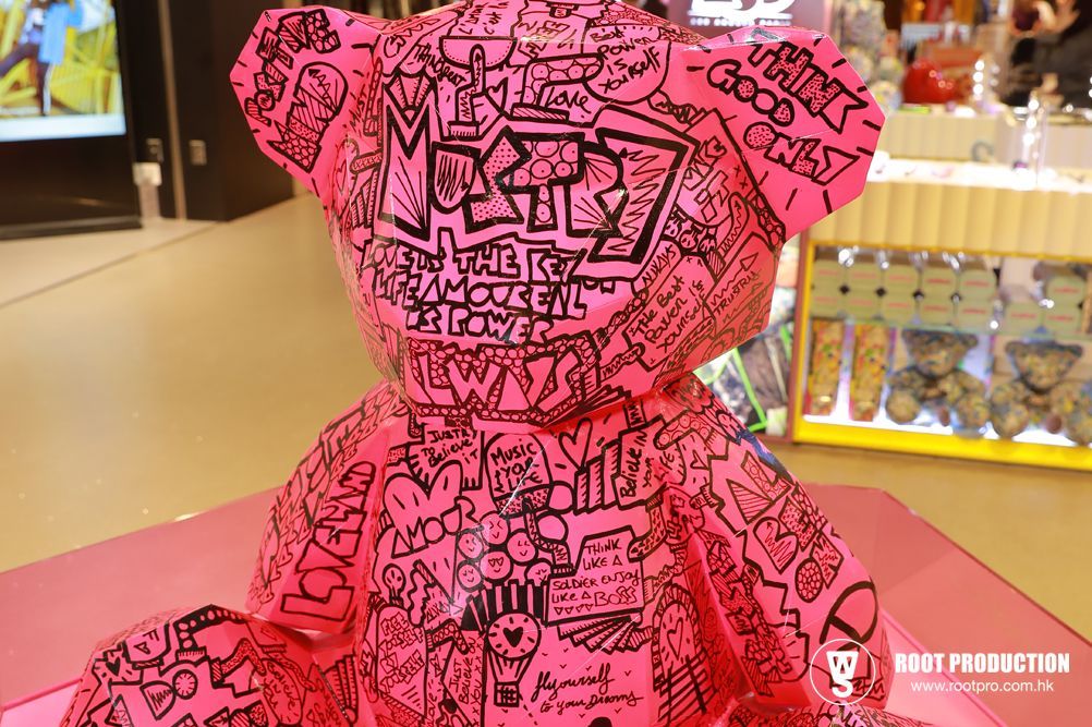 Pink teddy bear covered in black doodles, in a store setting.