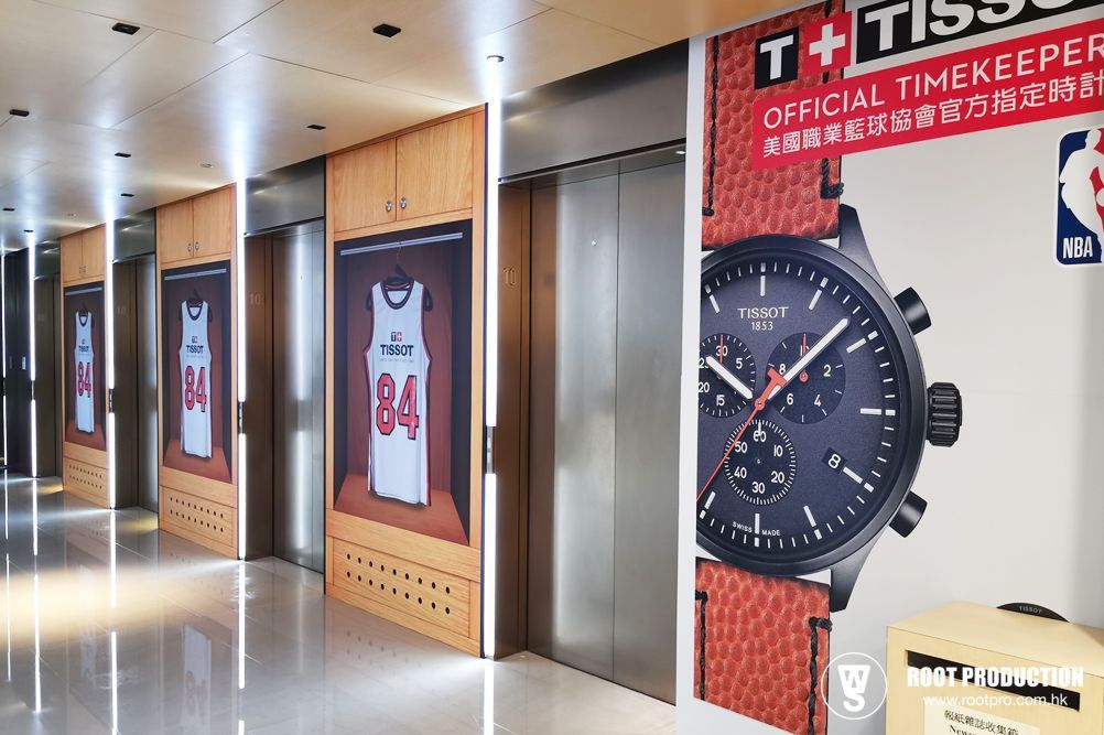 Elevator hall with watch ad and basketball jersey displays. Wooden panels, bright lights.