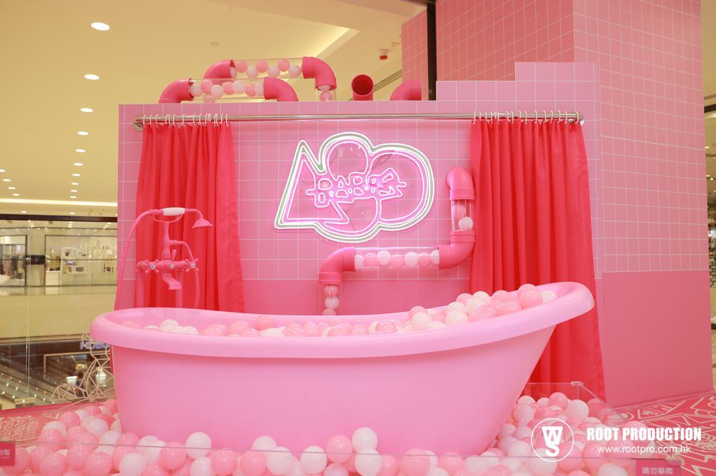 Pink bathtub display in mall with neon sign, pink tiles and curtains, filled with balls.
