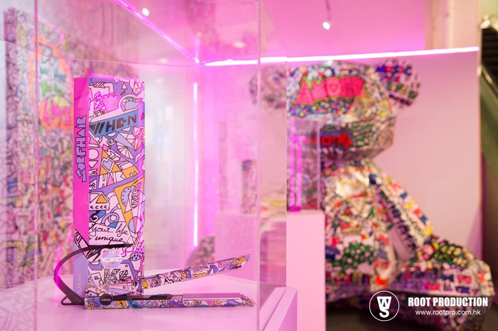A display with a colorful, patterned computer tower and a teddy bear sculpture, under pink lights.
