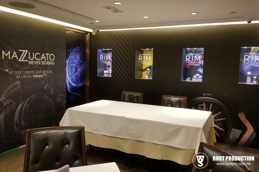 Mazzucato watch display area, showing a table covered with a white cloth, watch advertising, and chairs.