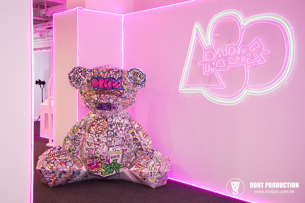 Giant mosaic teddy bear and neon sign in a pink-lit gallery setting.