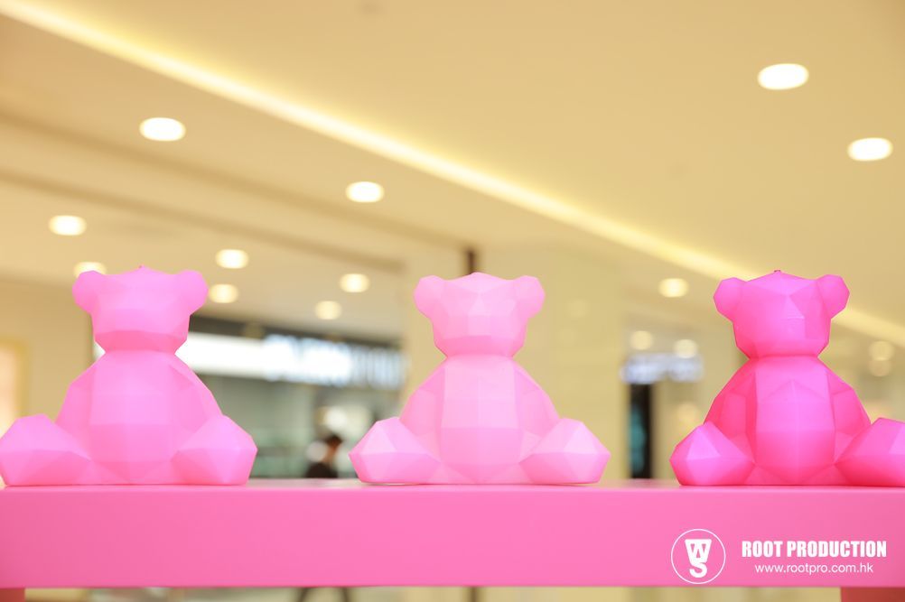 Three pink geometric teddy bear sculptures on a shelf, in a brightly lit indoor space.