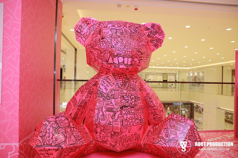 Giant pink bear sculpture in a shopping mall, covered with scribbled designs.