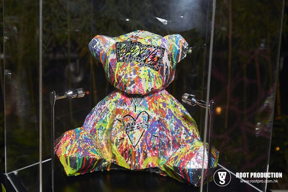 Colorful, paint-splattered teddy bear art inside a glass display case with a heart and writing detail.