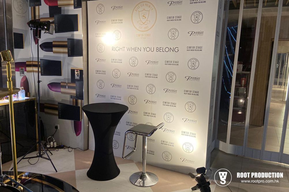 Event setup: white backdrop, black table & stool, makeup decor, gold accents, mirror on right.