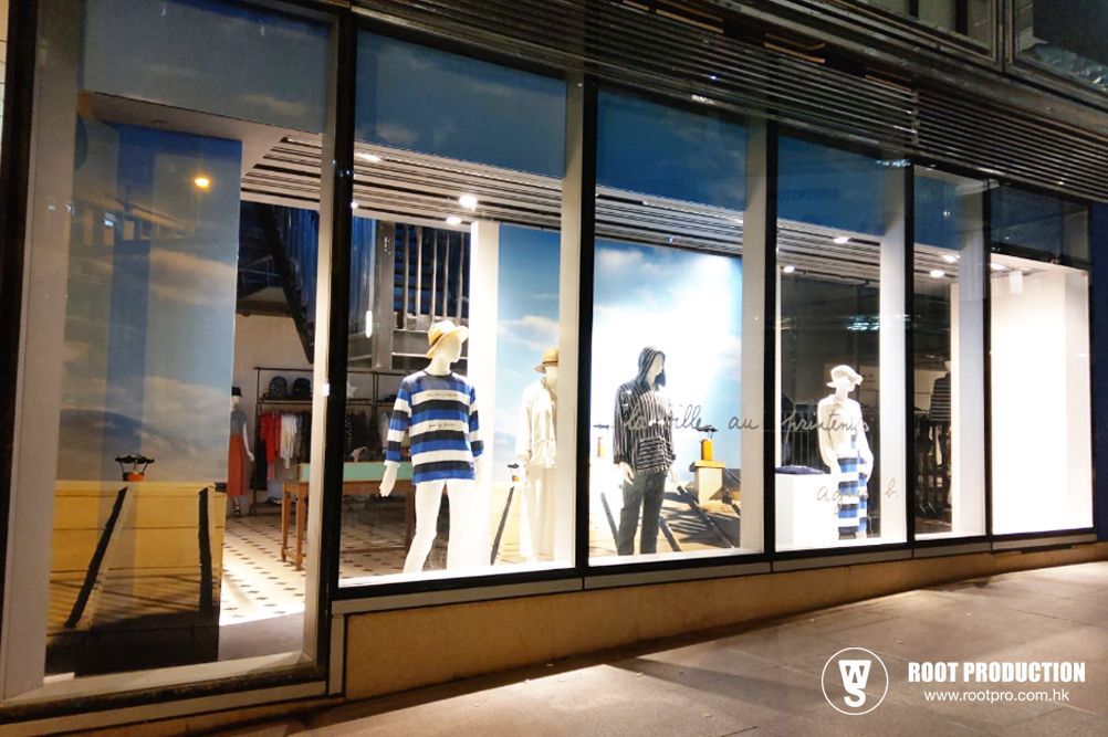 Storefront with mannequins wearing nautical-themed clothing, lit at night.